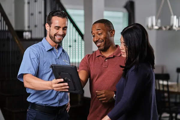 A smiling Mr. Electric electrician shows a tablet to a man and woman standing next to him. 